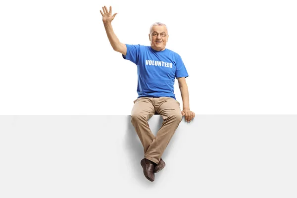 Mature man volunteer sitting on panel and waving — Stock Photo, Image