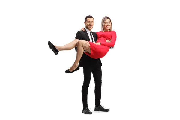Elegant man bär en kvinna i en röd klänning i famnen — Stockfoto