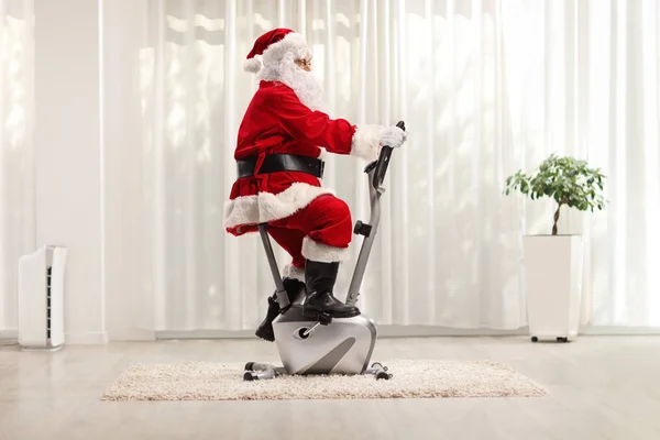 Santa Claus haciendo ejercicio en una bicicleta estacionaria — Foto de Stock