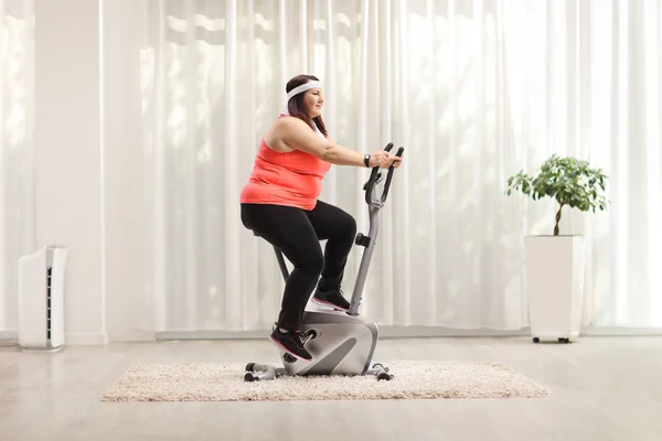 Overweight woman exercising on a stationary bike — Stock Photo, Image