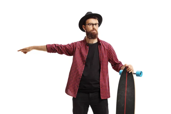 Hipster macho barbudo sosteniendo un longboard y apuntando en un dir —  Fotos de Stock