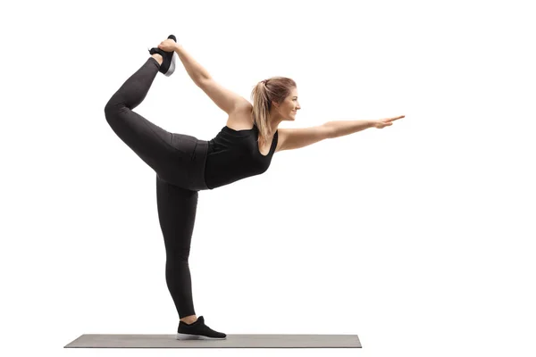 Young woman standing and stretching on an exercise mat — Stock Photo, Image