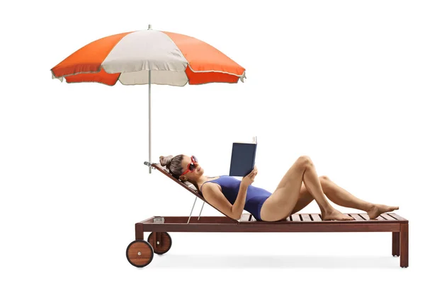 Молодая женщина в купальнике лежит на шезлонге с зонтиком — стоковое фото