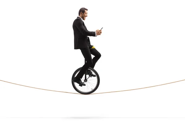 Happy businessman riding a unicycle on a rope and holding a mobi — Stock Photo, Image