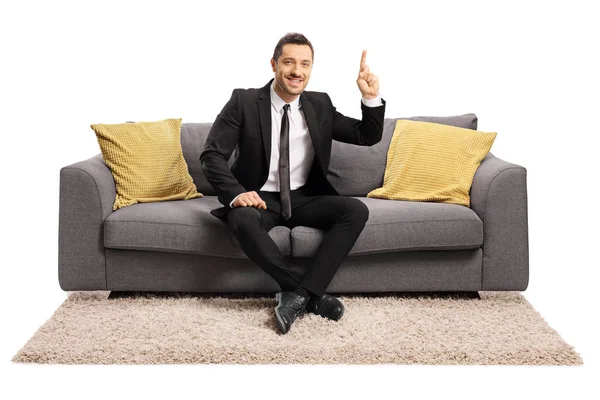 Ung man i en svart kostym sitter på soffan och pekar upp — Stockfoto