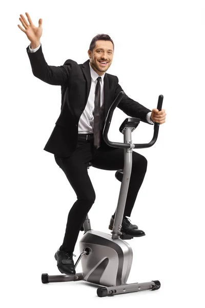 Sorrindo jovem empresário exercitando em uma bicicleta estacionária e wa — Fotografia de Stock