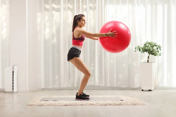 Молодая женщина держит фитнес-мяч и упражнения на дому — стоковое фото