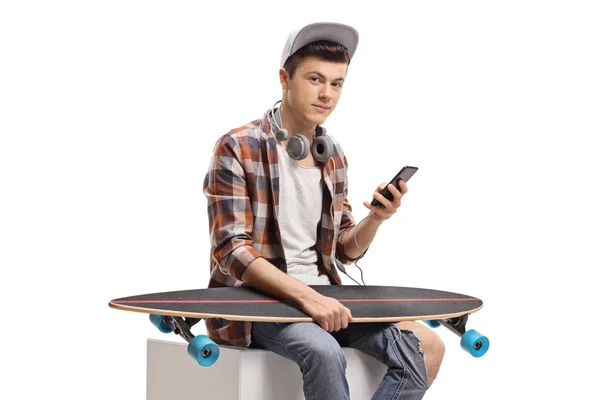 Mannelijke tiener schaatser met een telefoon en een Longboard sitting — Stockfoto