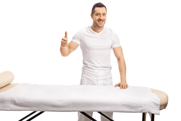 Massaggiatore professionale in piedi dietro un letto di massaggio e mostrando t — Foto Stock