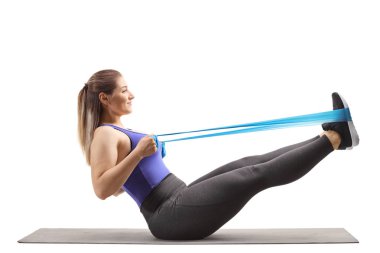 Genç kadın bir egzersiz m üzerinde elastik bir bant wih bacaklar germe