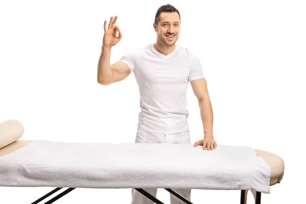 Profesional joven masajista de pie detrás de una cama de masaje y ges — Foto de Stock