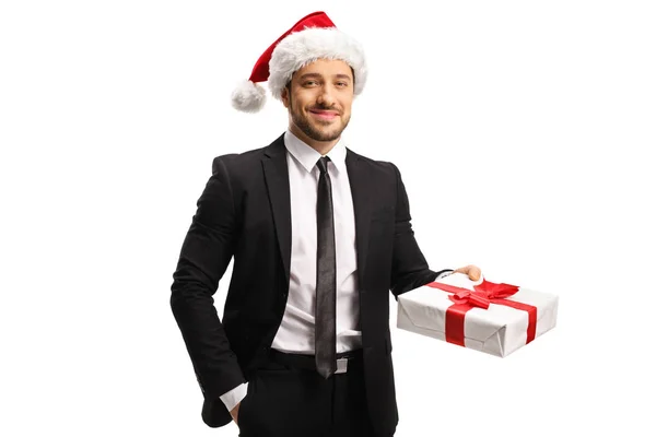 Jovem homem bonito em um terno com um chapéu de Natal segurando um pres — Fotografia de Stock