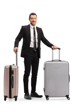 Takım elbiseli adam iki bavulla poz yapıyor.