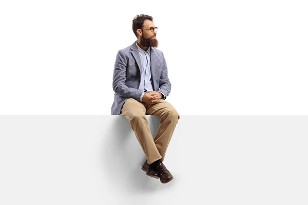 Hombre barbudo sentado en una pancarta blanca y mirando hacia un lado — Foto de Stock