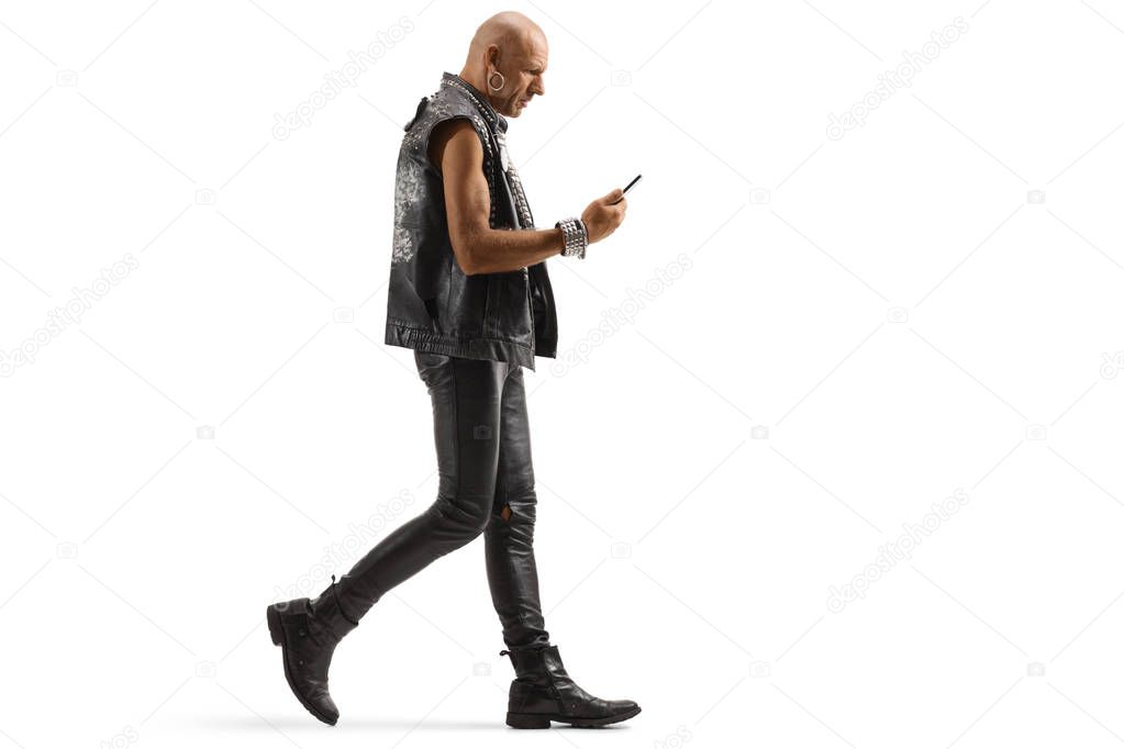 Bald punk in leather clothing waling and looking at his mobile p