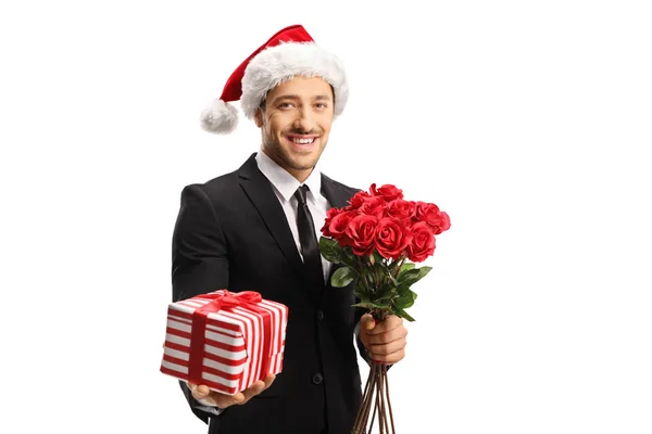 Giovane uomo elegante indossa un abito e un cappello di Babbo Natale che tiene rose un — Foto Stock