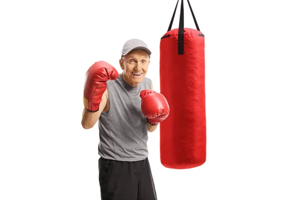 赤いボクシングの手袋と後ろにパンチングバッグを持つ高齢者 — ストック写真