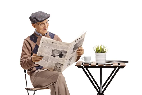 Senior sitter vid ett soffbord och läser en tidning — Stockfoto