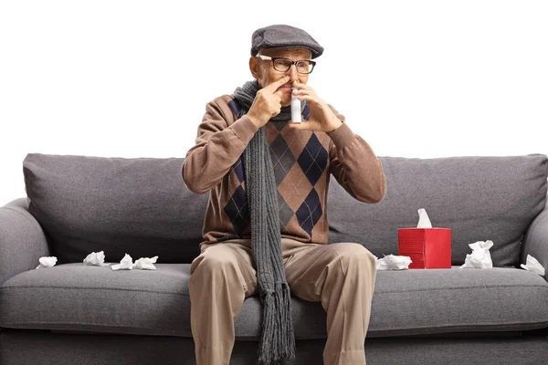 Reifer Mann sitzt auf einem Sofa und setzt sich ein Spray in die Nase — Stockfoto