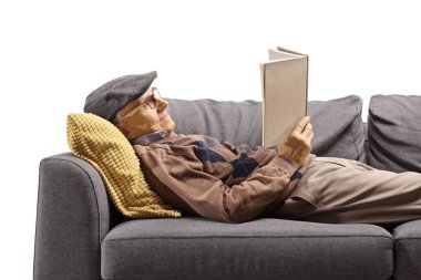 Yaşlı bir adam kanepede uzanıp kitap okuyor. 