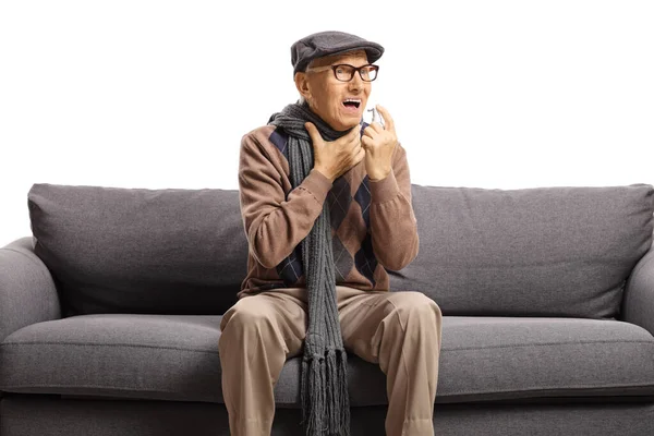 Älterer Herr mit Halsschmerzen, der auf einem Sofa sitzt und sprüht — Stockfoto