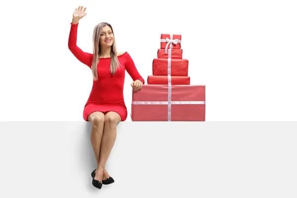 Jeune femme dans une robe rouge assise sur une bannière avec des cadeaux et — Photo