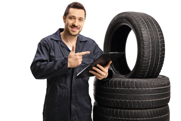 Mecánico de coche apuntando a una pila de neumáticos del vehículo y sosteniendo una c —  Fotos de Stock