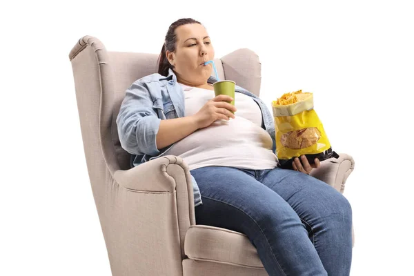Mujer con sobrepeso sentada en un sillón comiendo comida chatarra —  Fotos de Stock