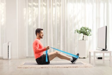 Adam evde lastik bir bantla TV karşısında egzersiz yapıyor.
