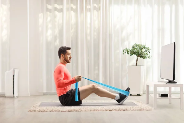 Man exercising with an elastic band in front of a tv at home