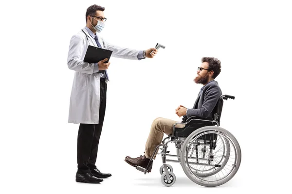 白地に隔離された車椅子の男に温度を測定する温度計を持つ男性医師の全長プロファイルショット — ストック写真