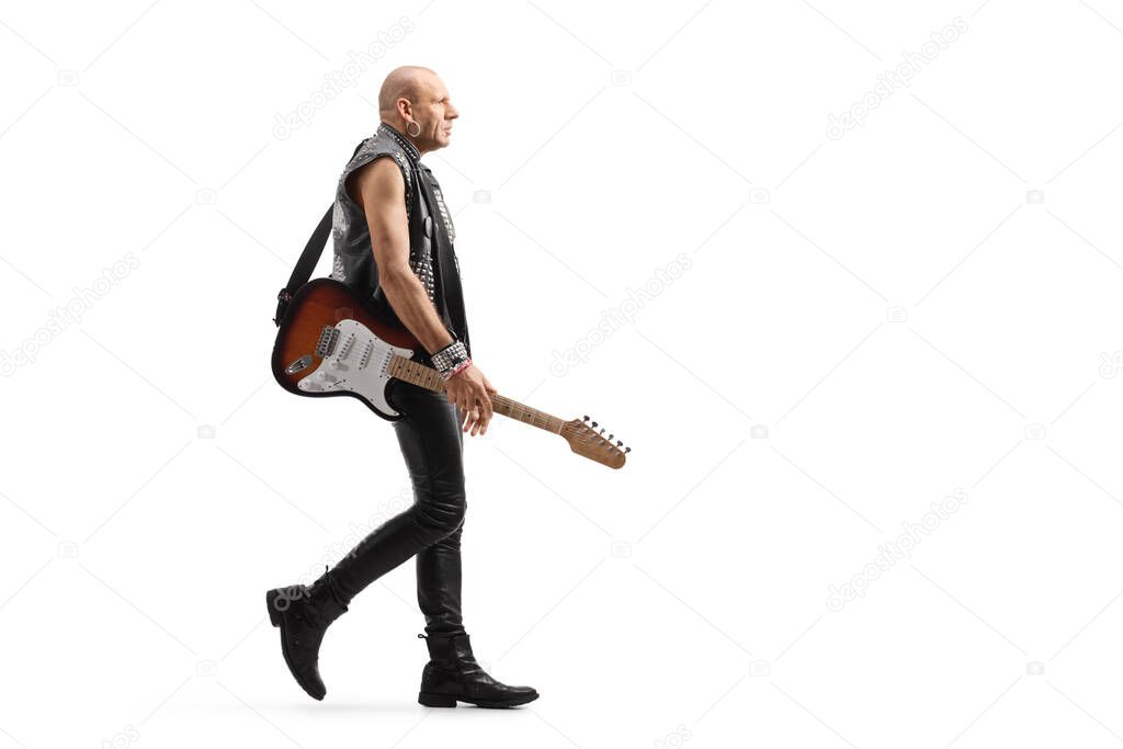Full length profile shot of a punk rocker musician with a guitar walking isolated on white background