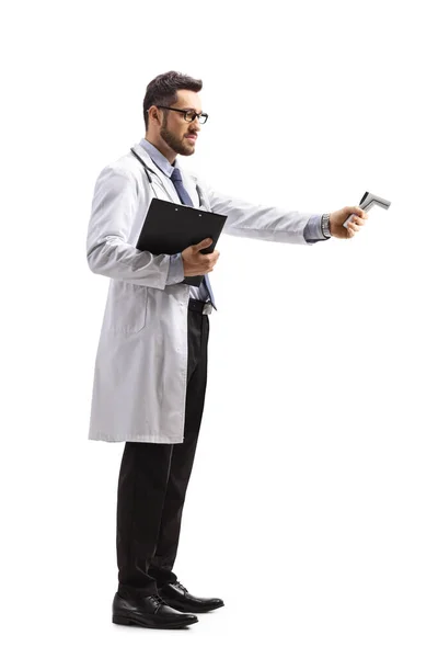 白い背景に隔離された遠くの温度計で温度を測定する男性医師の完全な長さプロファイルショット — ストック写真