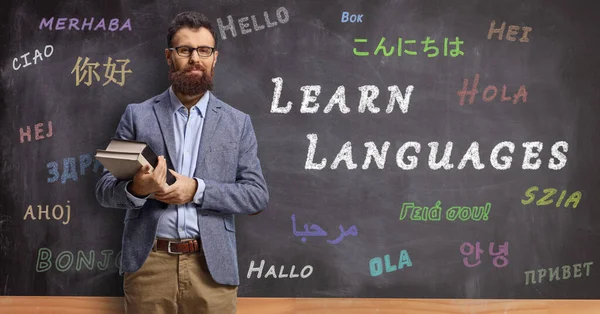 Male language teacher holding books and standing in front of a blackboard with text learn languages