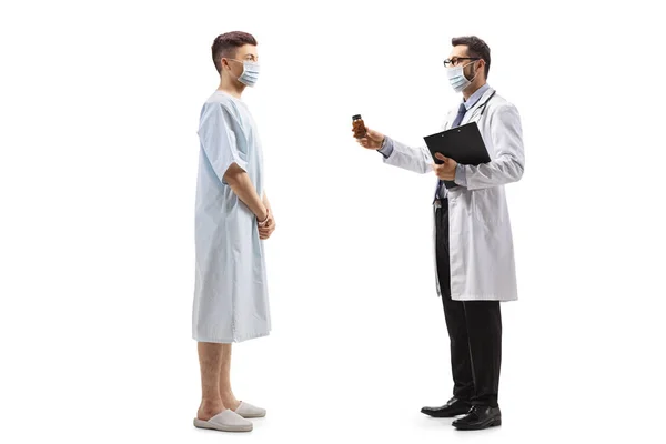 一名戴防护面罩的医生向一名身穿白衣的年轻男性病人提供药物的全景照片 — 图库照片