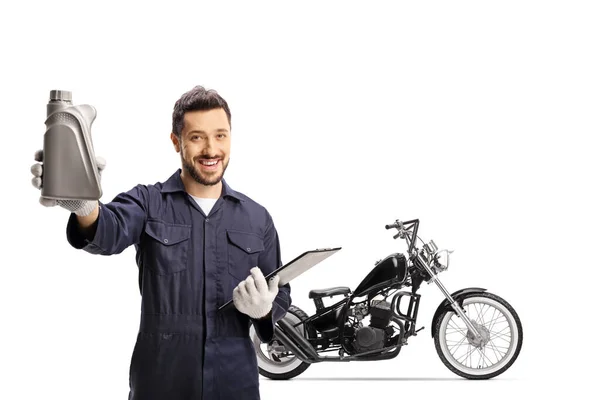 モーターオイルのボトルを保持し 白い背景に隔離されたチョッパーの横に立っているオートバイの整備士 — ストック写真