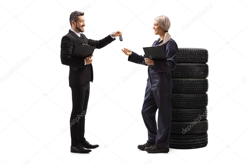 Full length profile shot of a businessman handing car keys to a female auto mechanic isolated on white background