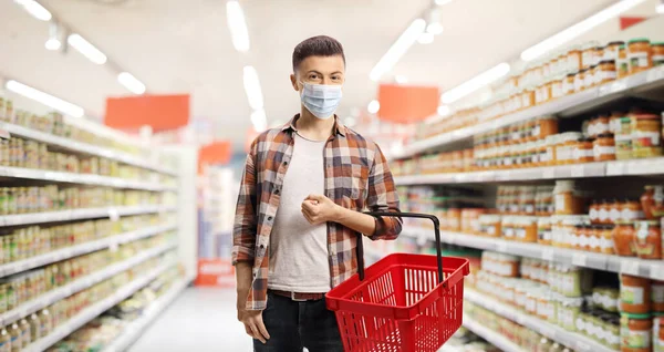 男でスーパーマーケットで保護顔マスクとショッピングバスケット — ストック写真