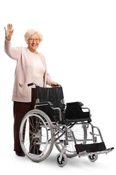Starsza Kobieta Popycha Pusty Wózek Inwalidzki Macha Przed Kamerą Odizolowana — Zdjęcie stockowe