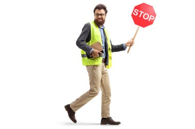 Güvenlik yeleği giymiş sakallı bir adamın trafik ışıklarıyla yürürken beyaz arka planda izole bir şekilde arkasını kolladığı uzun bir çekim.