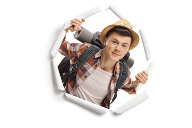 Sırt çantalı genç turist beyaz arka planda izole edilmiş kağıttan bir delikten bakıyor.
