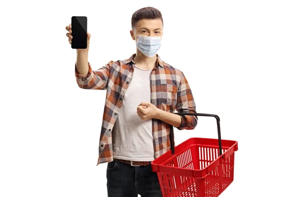 一个戴着防护面罩和一个空购物篮的年轻人 拿着一部手机对着摄像机 背景是白色的 — 图库照片