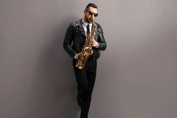 Hombre Una Chaqueta Cuero Tocando Saxofón Apoyado Una Pared Gris —  Fotos de Stock