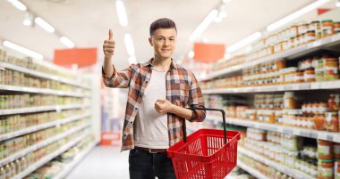 Genç adam süpermarkette alışveriş yapıyor ve baş parmağını kaldırıyor.