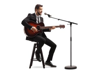 Elektrikli gitarlı genç bir erkek müzisyen bir sandalyede oturuyor ve beyaz arka planda soyutlanmış bir şekilde çalıyor.