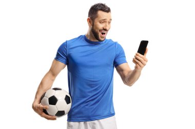Şaşırmış futbolcu bir top tutuyor ve beyaz arka planda izole edilmiş bir cep telefonuna bakıyor.