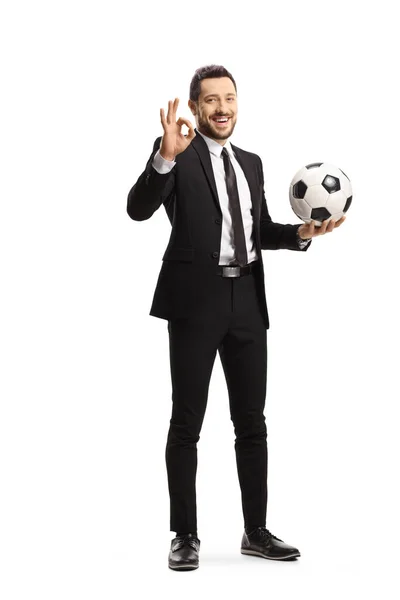 サッカーを保持している黒のスーツの男の完全な長さの肖像画とジェスチャーOkサインは白の背景に隔離 — ストック写真