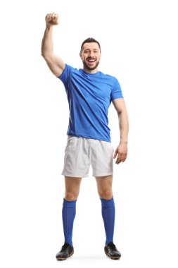 Mavi şortlu ve beyaz şortlu bir futbolcunun tam boy portresi beyaz arka planda izole bir el kaldırıyor.