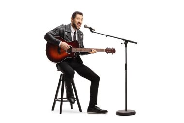 Akustik gitar çalan ve beyaz arka planda izole edilmiş bir mikrofonda şarkı söyleyen bir adam.