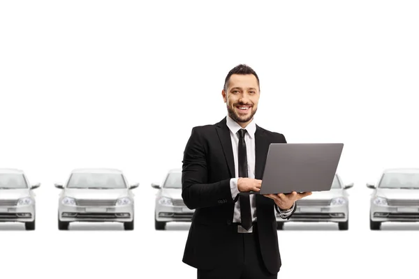 汽车推销员在笔记本电脑上工作 在白色背景隔离的银色汽车前对着相机微笑 — 图库照片